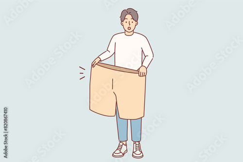 Lost weight man with big shorts in hands is surprised at size of own clothes from past