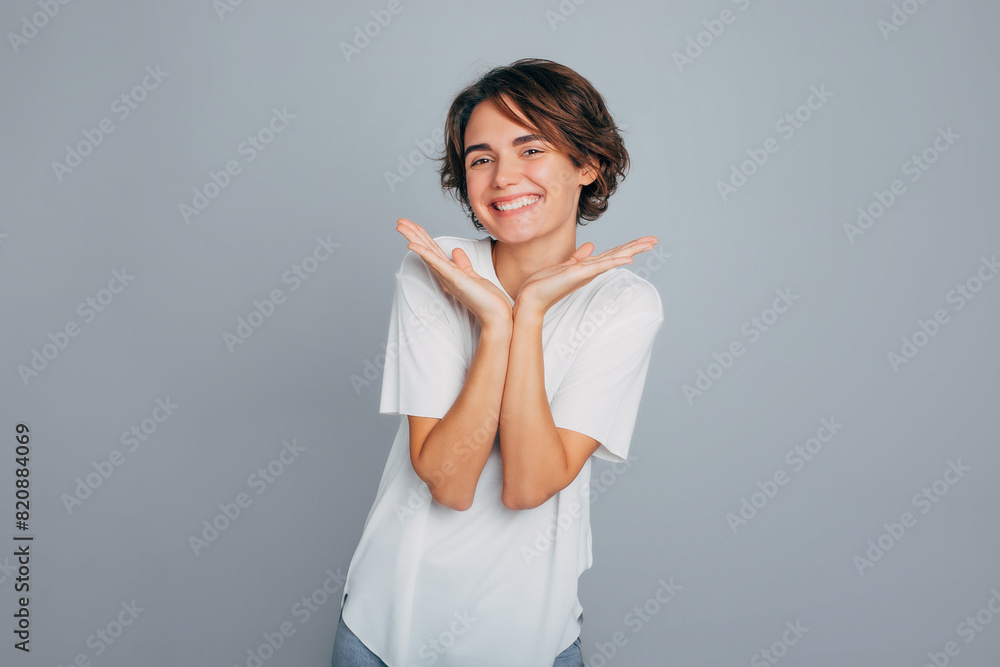 Photo of attractive smiling young female with healthy skin and modern hairstyle in good mood posing on a grey wall background Photo of attractive smiling young female with healthy skin and modern hairstyle in good mood posing on a grey wall background