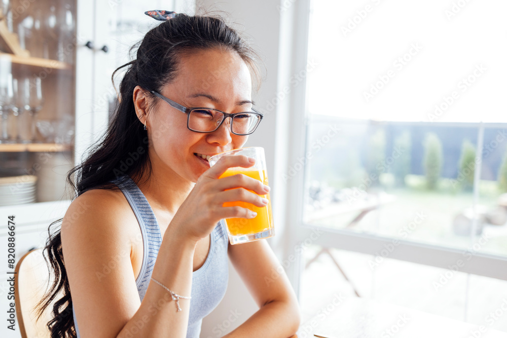 A smiling attractive Asian woman drinks freshly squeezed orange juice A smiling attractive Asian woman drinks freshly squeezed orange juice