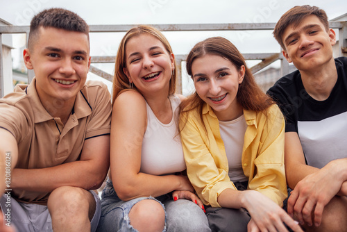 Four cute teenagers taking a selfie. Funny friends takes a picture of theyself on the phone outdoors. Smiling boys and girls sitting on the street. © Dasha Petrenko