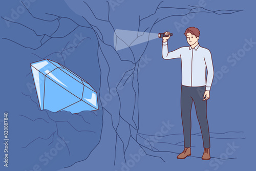 Business man found treasure or diamond inside cave, symbolizing reward for courage and ambition. White-collar guy with flashlight in hands does not see treasure because of thin partition