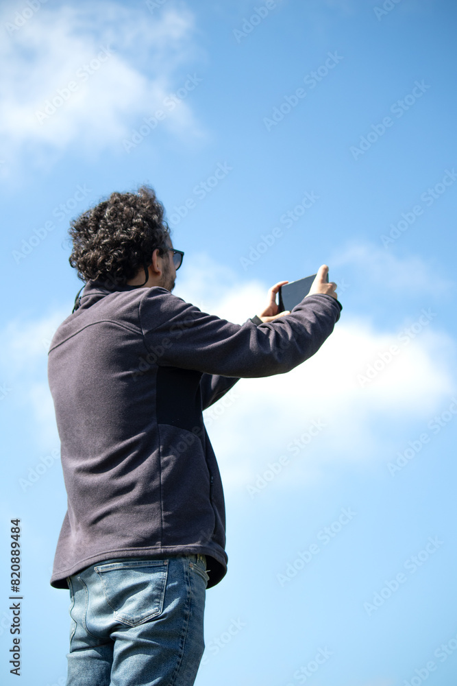 Turkish man taking photo with mobile phone on blue sky background. Turkish man taking photo with mobile phone on blue sky background.