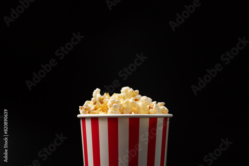 Popcorn bucket, cinema entertainment, salted snack, classic cardboard, black background, copy space © yta