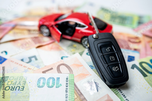 Small red toy car with black key on pile of euro bills