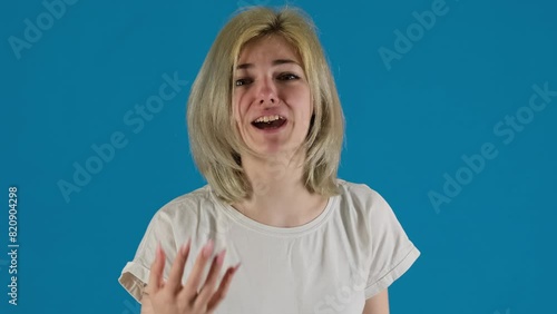 Female student looks upset arguing with friend on blue background. Desperate woman feels negative emotions during communication photo