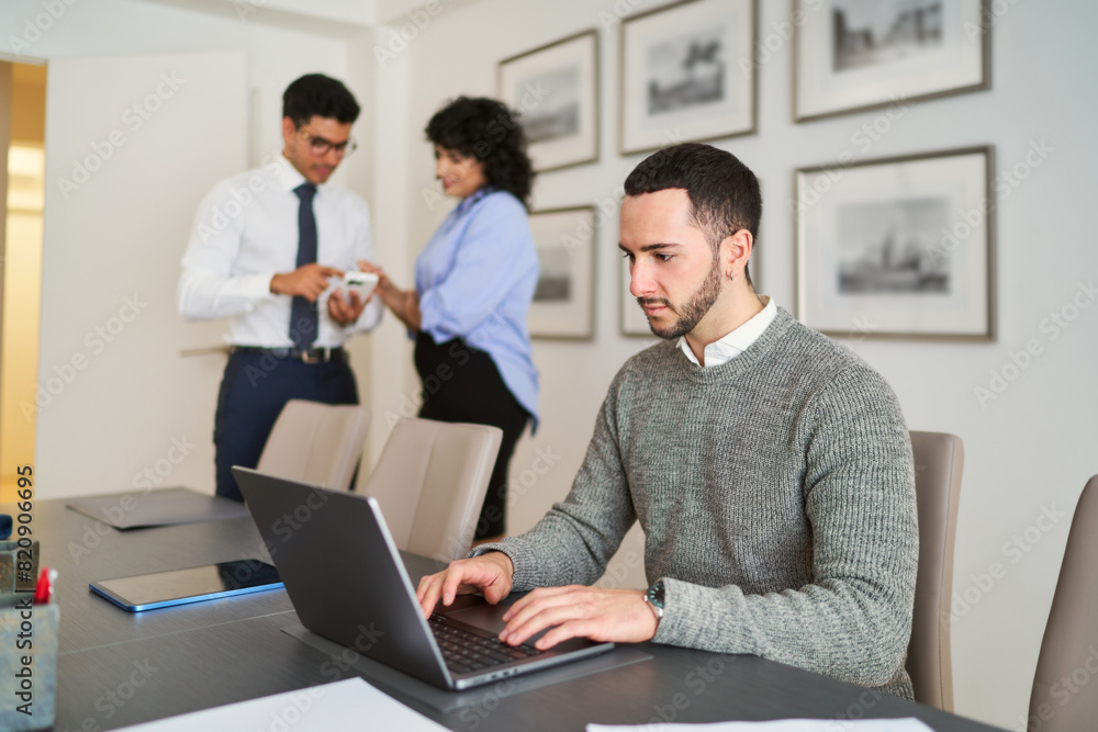A man is typing on a laptop in front of a woman and a man A man is typing on a laptop in front of a woman and a man