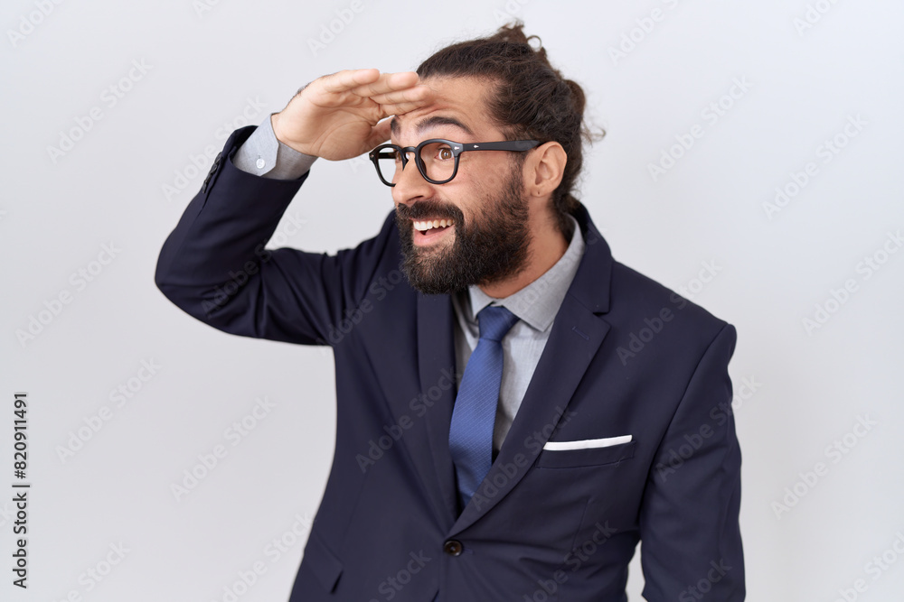 Hispanic man with beard wearing suit and tie very happy and smiling looking far away with hand over head. searching concept. Hispanic man with beard wearing suit and tie very happy and smiling looking far away with hand over head. searching concept.
