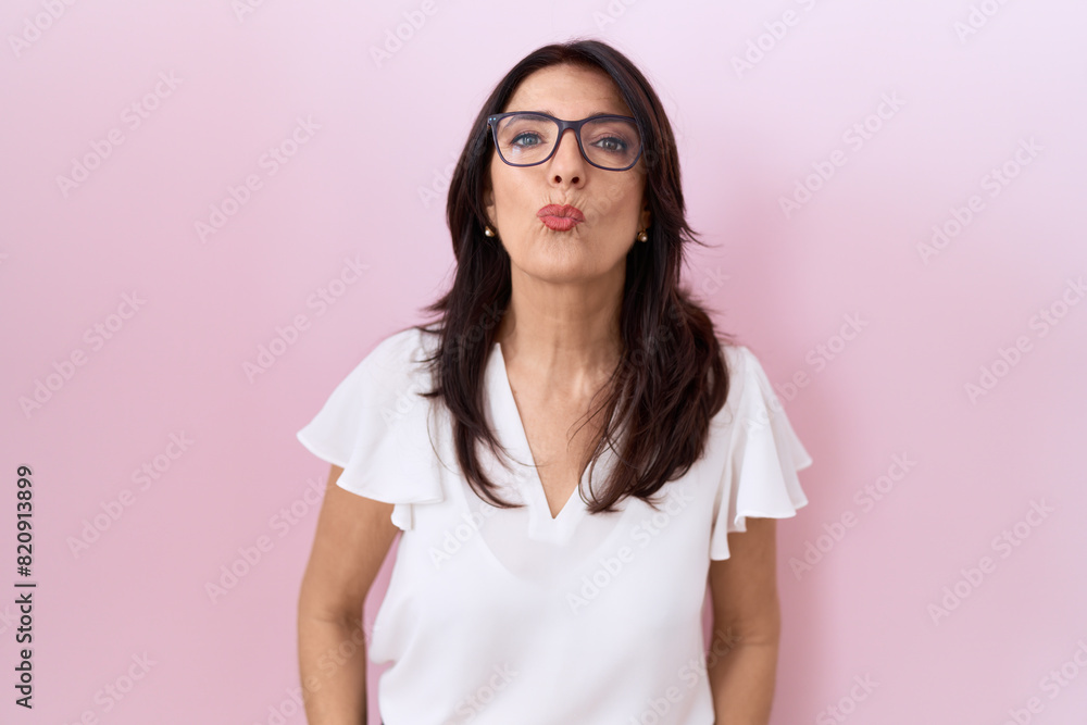 Middle age hispanic woman wearing casual white t shirt and glasses looking at the camera blowing a kiss on air being lovely and sexy. love expression.