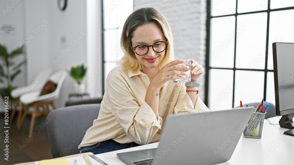 Fototapeta premium Young blonde woman business worker using laptop drinking water at the office