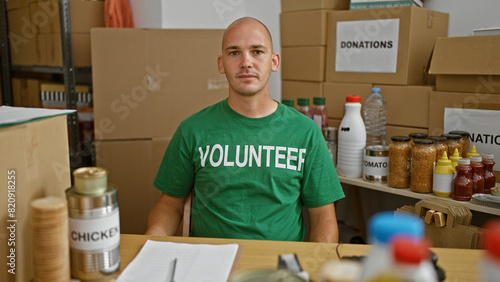 Young hispanic man volunteer sitting on table with serious face at charity center