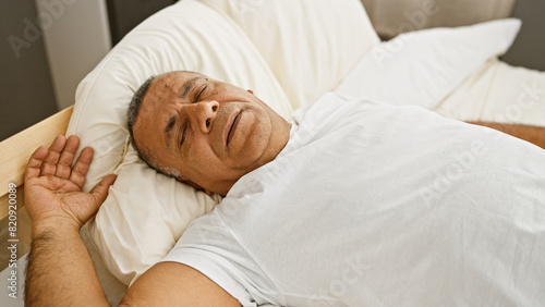 A middle-aged hispanic man rests peacefully in a bright bedroom setting, epitomizing relaxation and domestic comfort. photo