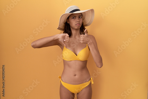Young hispanic woman wearing bikini and summer hat doing thumbs up and down  disagreement and agreement expression. crazy conflict