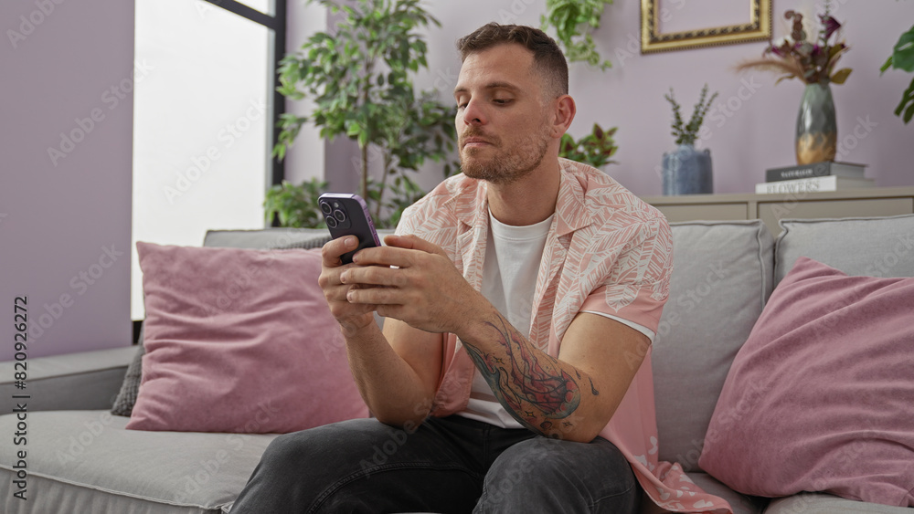 Handsome man with tattoos using smartphone in modern living room Handsome man with tattoos using smartphone in modern living room