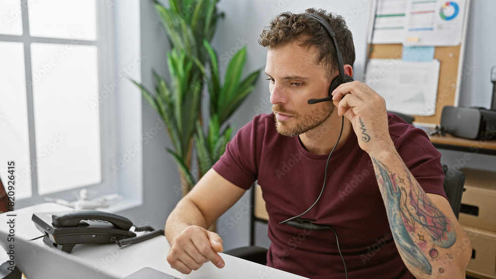 Fototapeta premium A young hispanic man with a beard works in an office, wearing a headset for communication.