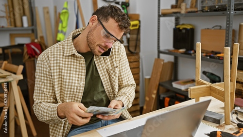 Quadro em tela Handsome man counting money multitasking with a phone call in a woodworking workshop