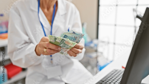 Middle-aged female doctor counts hong kong dollars indoors, highlighting healthcare costs. photo