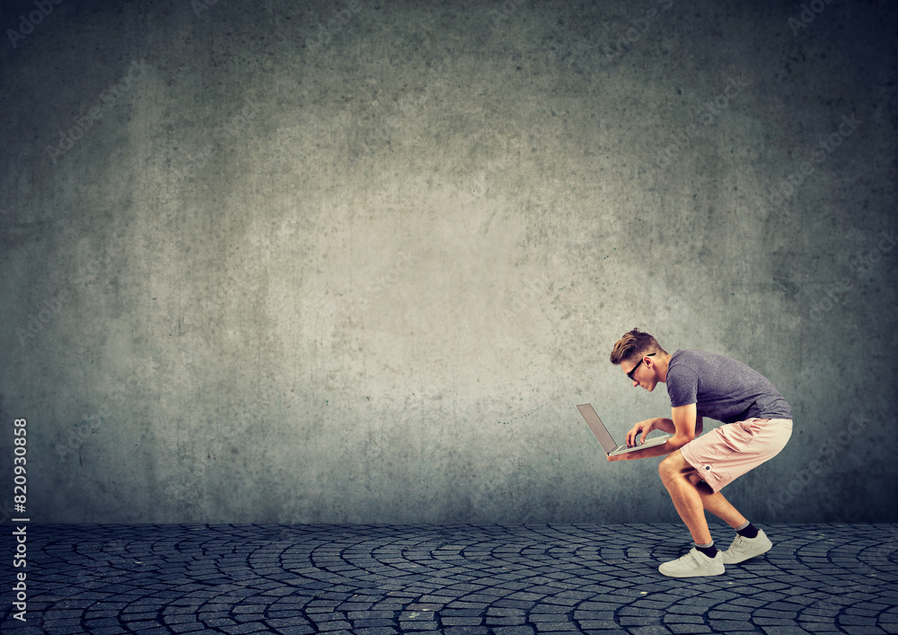 Young man with laptop crouches looking for Wi-Fi signal Young man with laptop crouches looking for Wi-Fi signal