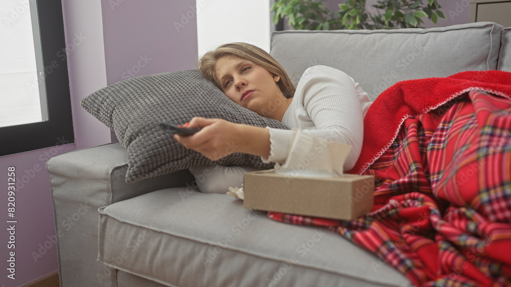 Sick woman reclining on couch with tissues and remote, covered in blanket, in a home interior Sick woman reclining on couch with tissues and remote, covered in blanket, in a home interior