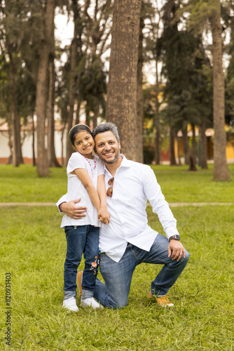 A man and a little girl are posing for a picture in a park