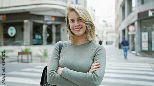 Photo: Portrait of a confident young adult caucasian woman with short blonde hair, crossing arms on a city street outdoors. Portrait of a confident young adult caucasian woman with short blonde hair, crossing arms on a city street outdoors.