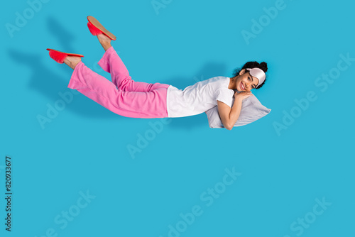 Full body portrait of pretty young woman levitate pillow wear pajama isolated on blue color background