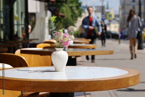 Street cafe in city with empty tables outdoor. Vases of flowers on round tables and cozy chairs in sunny day