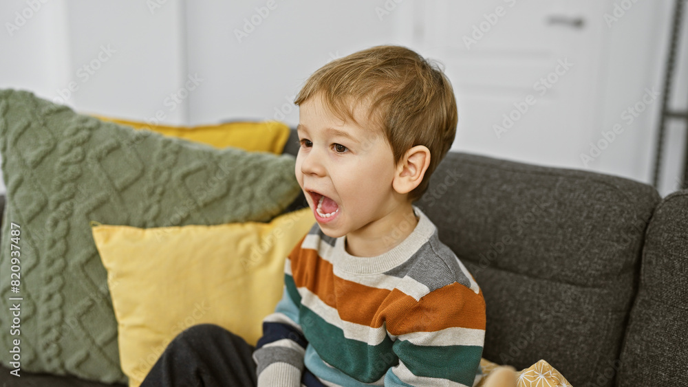 Fototapeta premium Young caucasian boy yelling while sitting on a gray sofa in a cozy living room setting