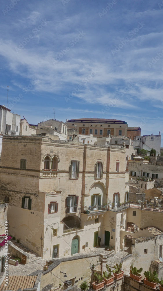 Old stone buildings with green shutters under a clear blue sky in matera, basilicata, italy, displaying historic architecture and mediterranean charm in an outdoor town setting. Old stone buildings with green shutters under a clear blue sky in matera, basilicata, italy, displaying historic architecture and mediterranean charm in an outdoor town setting.