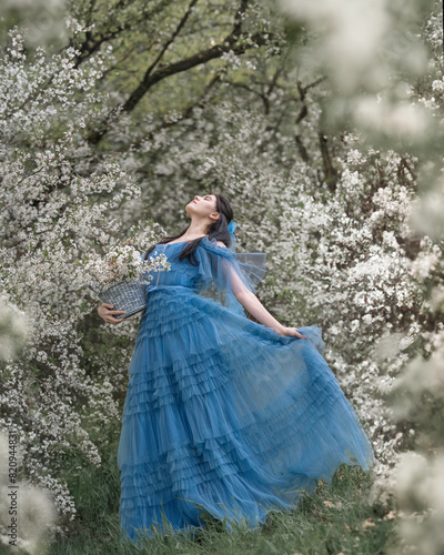 A girl in a blue dress dancing in a blooming cherry orchard