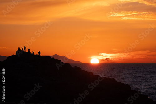 Silhouette of a group of people on a hill watching sunset over sea