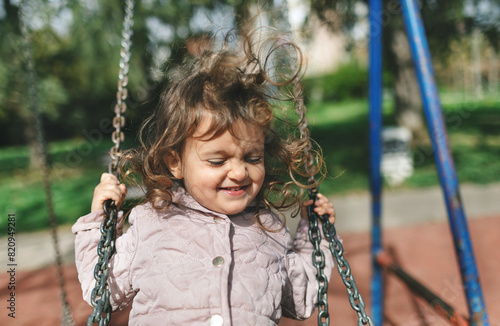Littler girl swing and laughing at playground. Happy toddler kid playing.