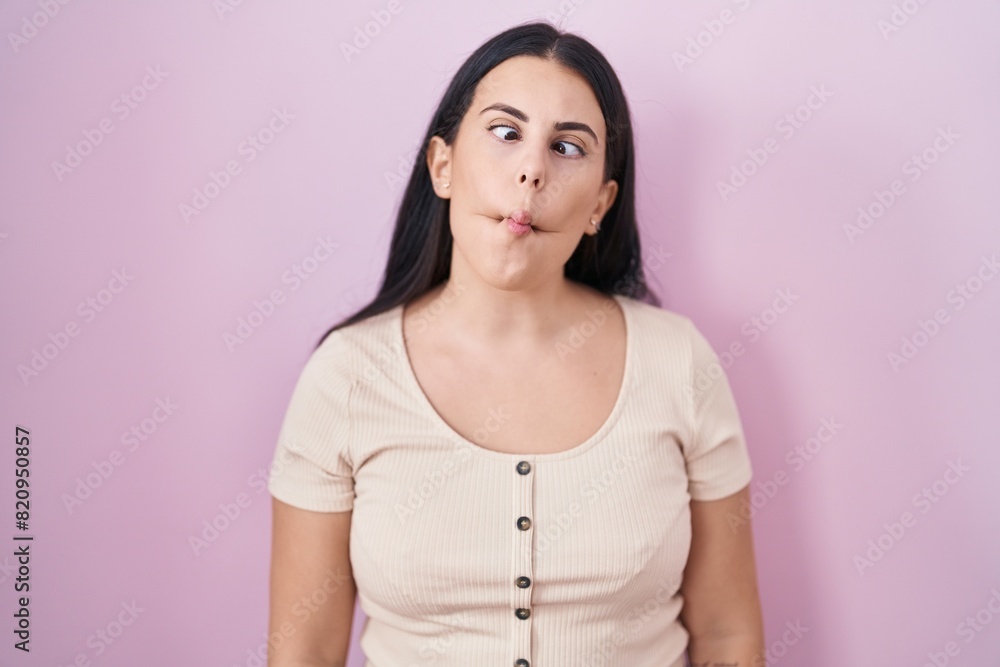 Young hispanic woman standing over pink background making fish face with lips, crazy and comical gesture. funny expression. Young hispanic woman standing over pink background making fish face with lips, crazy and comical gesture. funny expression.