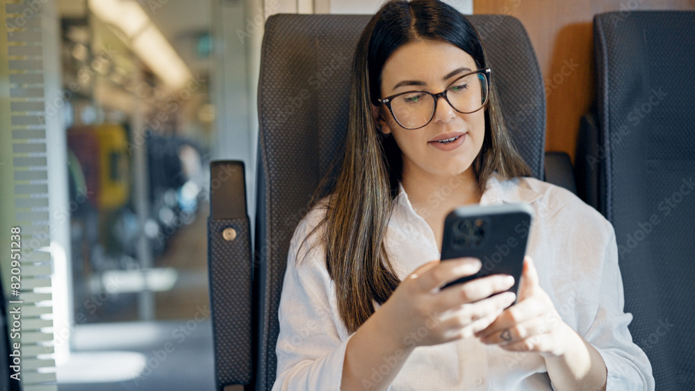 Young beautiful hispanic woman using smartphone sitting inside train wagon