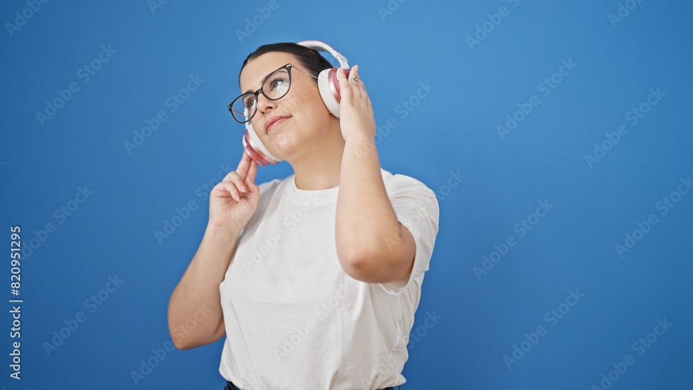Young beautiful hispanic woman dancing wearing headphones over isolated blue background Young beautiful hispanic woman dancing wearing headphones over isolated blue background