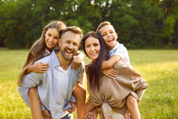 Happy family having a good time together in nature. Portrait of a cheerful father and mother piggy backing their cute children on a green meadow in a beautiful summer park 