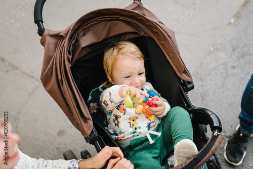 Little boy sitting fastened in a stroller. Family walk time with baby carriage in park. Closeup.