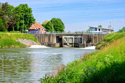 Photo of a boa lock with water flowing out. (Netekanaal in Viersel, Belgium). Blue sky with clouds.