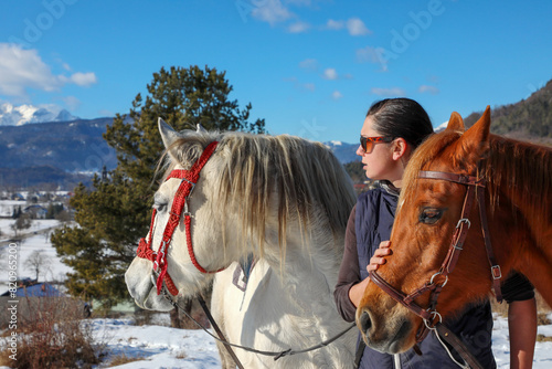 A girl in sunglasses and next to her two horses, white and bay.