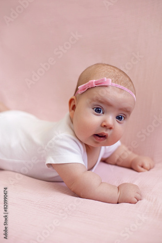 girl baby infant with a bow lies on the bed in a white bodysuit the child is 4 months old