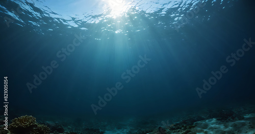 Sunlight filters through the dark blue depths of the ocean  illuminating the seabed and creating a serene underwater scene.