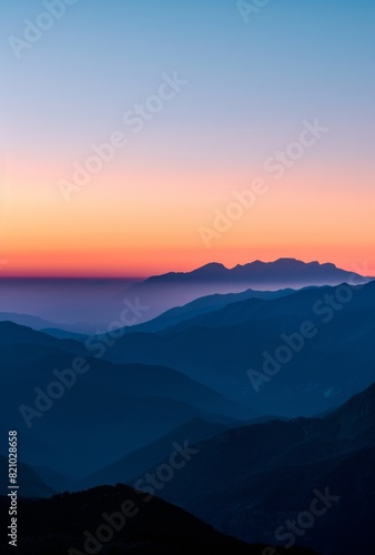 A breathtaking sunrise over the mountains, casting an orange and blue glow on their silhouette against a clear sky.