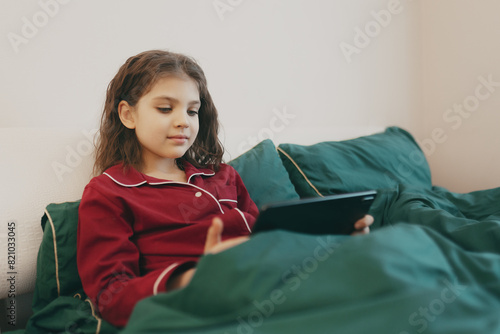 Girl in homemade pyjamas sitting in bed looking at tablet, lifestyle.