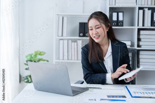 Sharing good business news. Attractive young businesswoman talking on the mobile phone and smiling while sitting at her working place in office and looking at laptop PC. © Tj