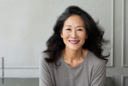 Portrait of a grinning asian woman in her 50s smiling at the camera isolated on minimalist or empty room background