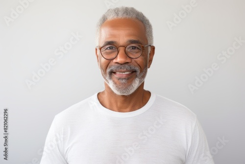 Portrait of a grinning afro-american man in his 80s with arms crossed while standing against minimalist or empty room background