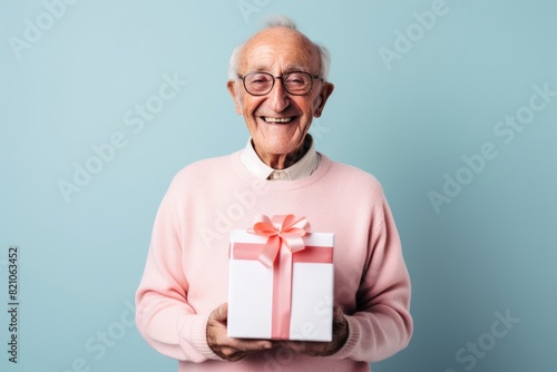 Portrait of a grinning man in his 80s holding a gift while standing against minimalist or empty room background © Markus Schröder