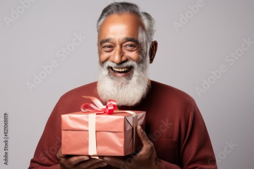 Portrait of a blissful indian man in his 60s holding a gift in front of minimalist or empty room background © Markus Schröder