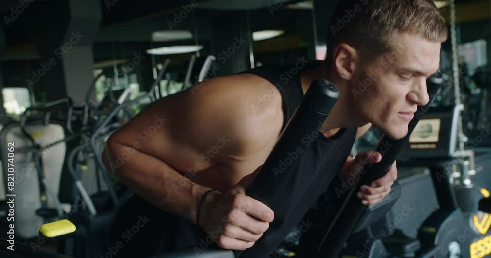 A focused young man exercising on an elliptical machine in a gym, showing intensity and determination during his workout. Determined Young Man Working Out Intensely on an Elliptical Machine A focused young man exercising on an elliptical machine in a gym, showing intensity and determination during his workout. Determined Young Man Working Out Intensely on an Elliptical Machine