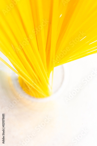 A bunch of bright yellow spaghetti arranged in a glass on a clean white surface, top view