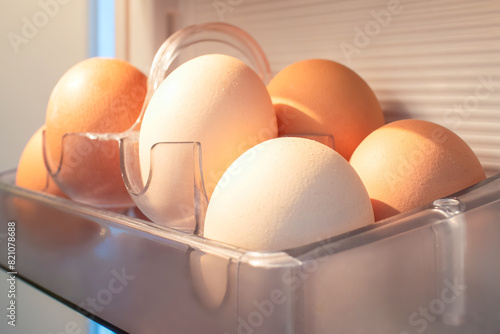 Organic eggs are stored in a transparent container inside a fridge, used as a key ingredient in various dishes, an oval staple food in different cuisines